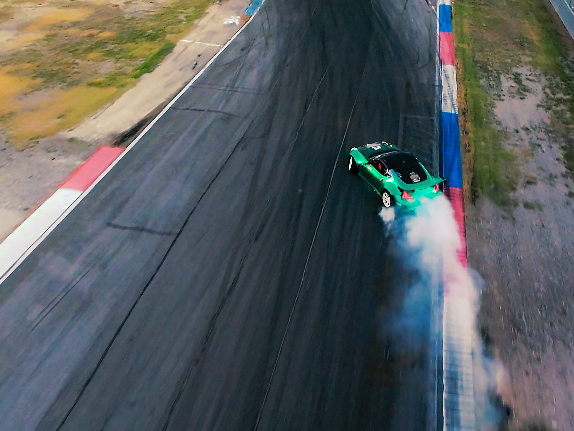 FPV drone view from above of a drift car trailing tire smoke through a corner at golden hour, Texas Motor Speedway