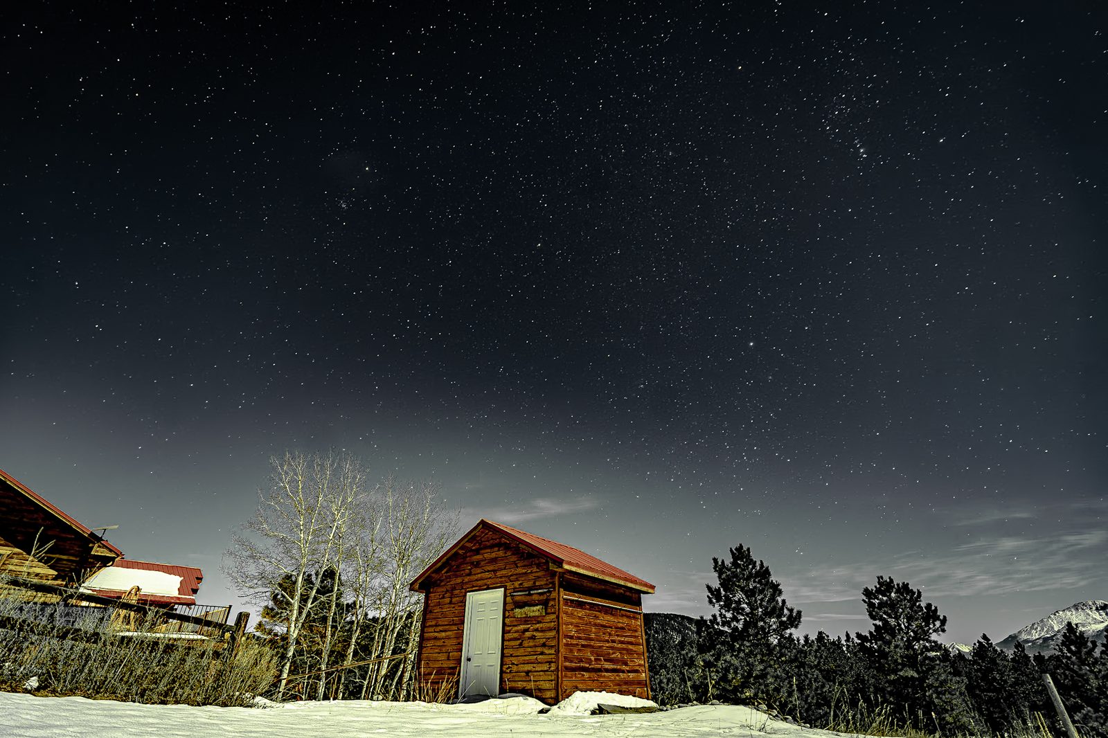 Small red-roofed cabin in snow under a sky full of stars